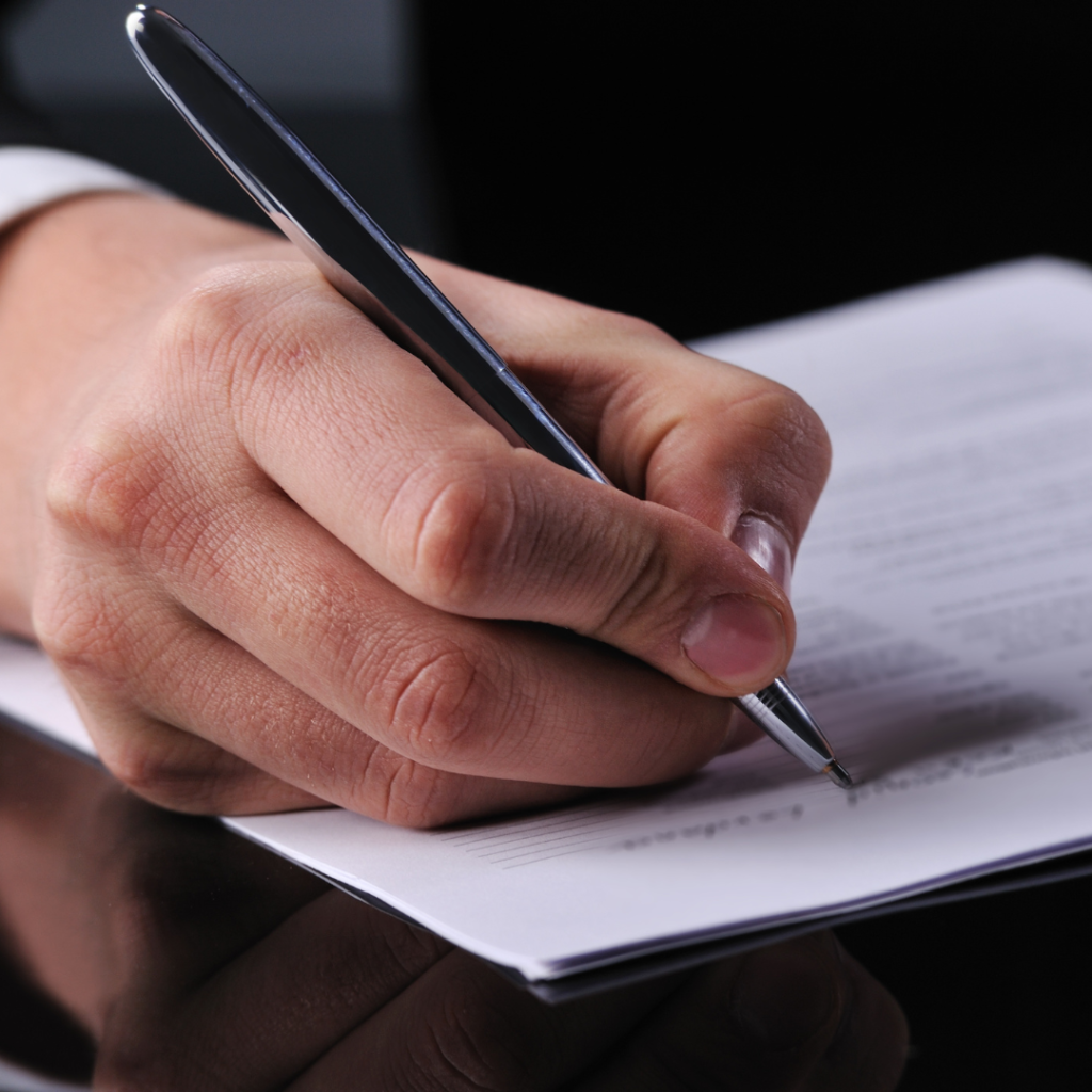 The hand of a white male using a black ballpoint pen to write on a piece of paper. Apprenticeship Connect Policies.
